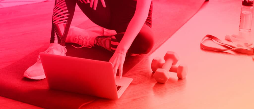 woman sitting on yoga mat looking at her laptop with dumbbells next to her