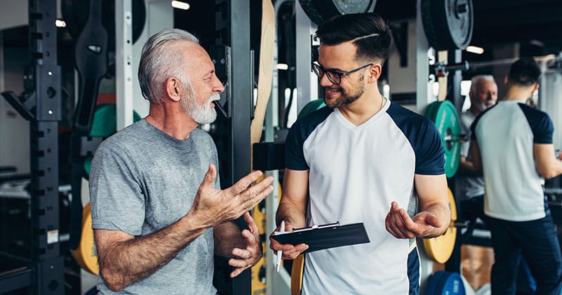 Personal trainer talking to older man in gym