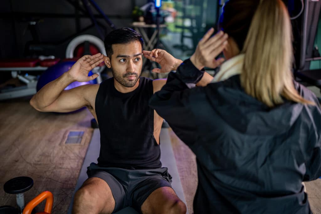 Woman coaching a man how to do sit-ups in a gym setting