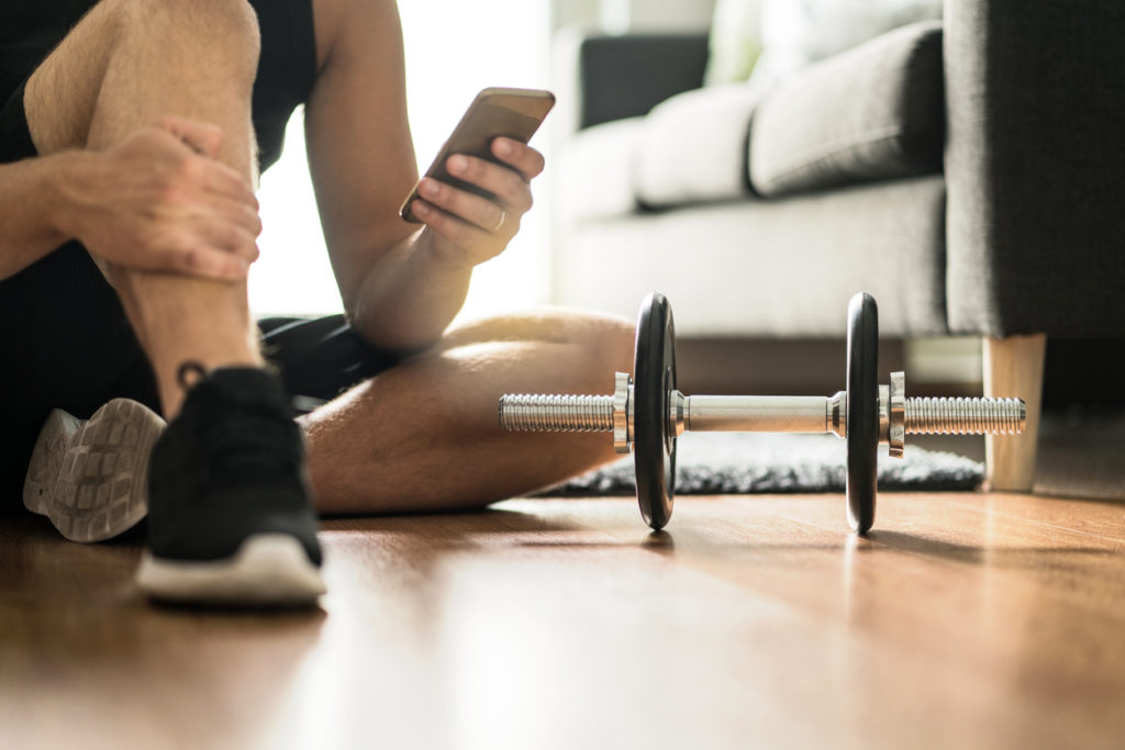 Man using smartphone during workout at home. Online personal trainer or on mobile phone. Internet fitness class or video course.