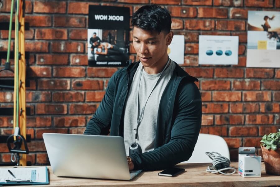 Cropped shot of a young male fitness instructor using a laptop while working in a gym