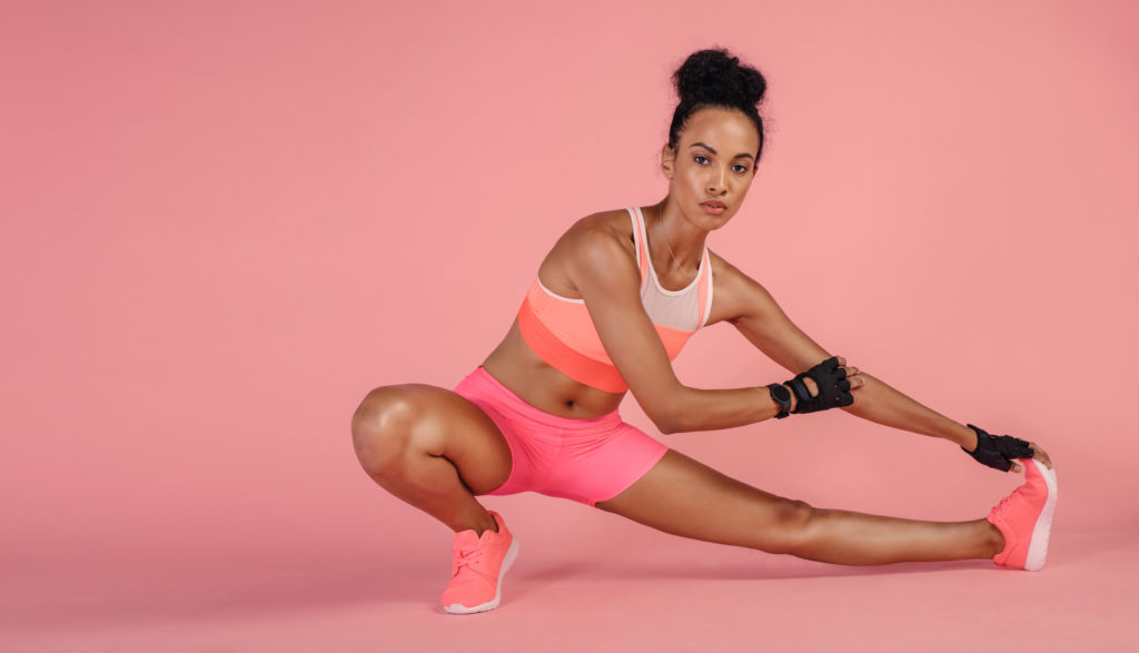 Woman in sportswear working out on pink background. Healthy woman doing stretching exercises in studio.