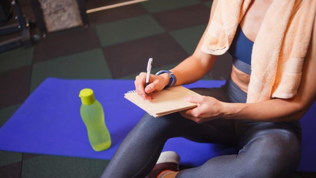 Personal trainer sitting in a gym writing her bio in a note pad. 