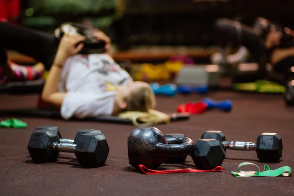 Free weights on a gym floor with a woman exercising in the background