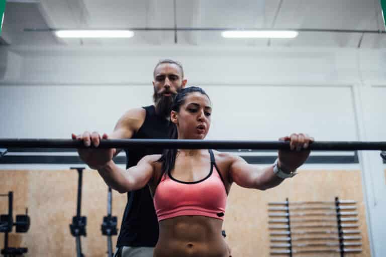 Young woman power lifting helped by her personal trainer.
